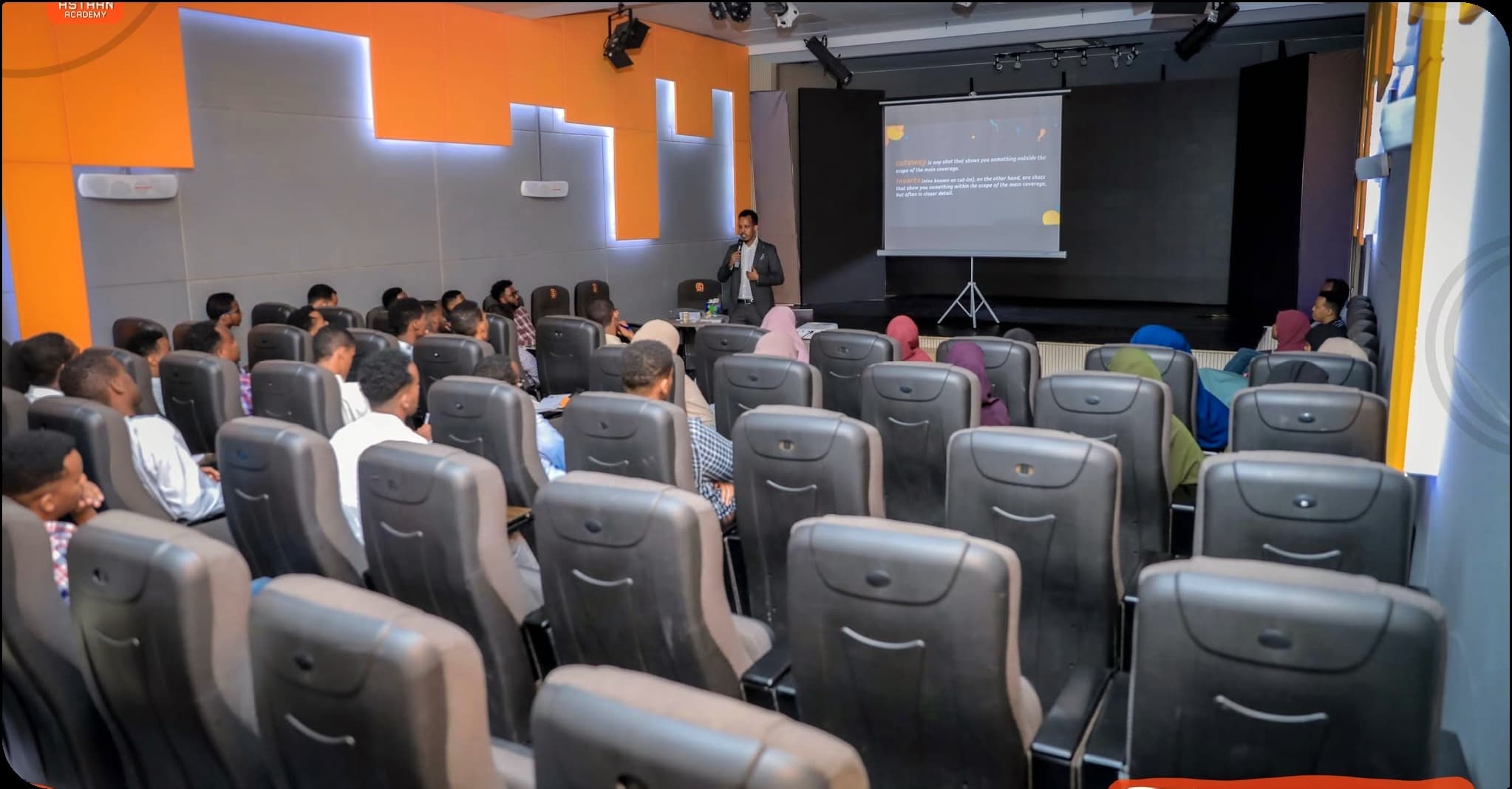 Students seated in the Astaan Academy screening room watch an instructor present a video editing lesson
