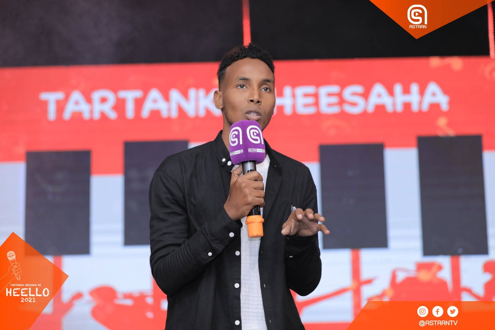 Contestant in a black shirt singing into a purple Astaan microphone in front of a red Tartanka Heesaha stage banner