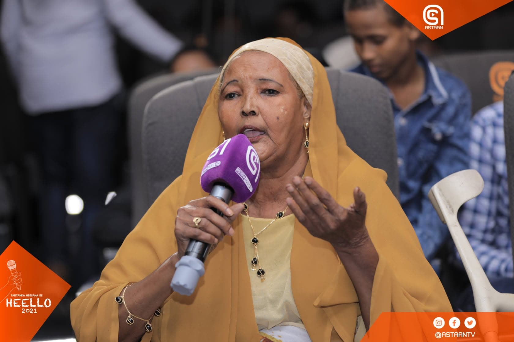 Audience member in a gold hijab speaking into a purple Astaan microphone from the studio seats