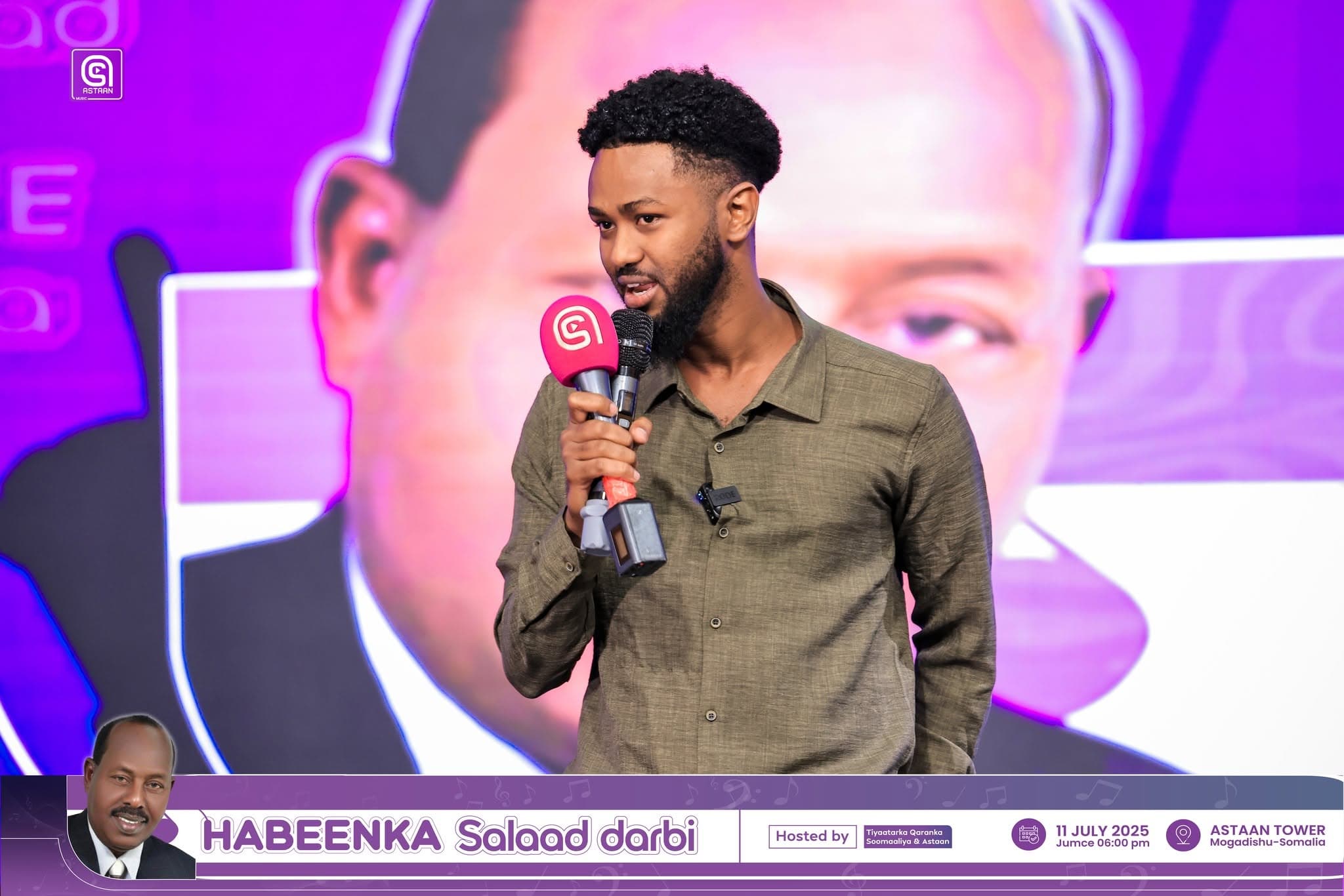 A young MC speaks into a pink Astaan microphone in front of the purple Habeenka Salaad Darbi backdrop.