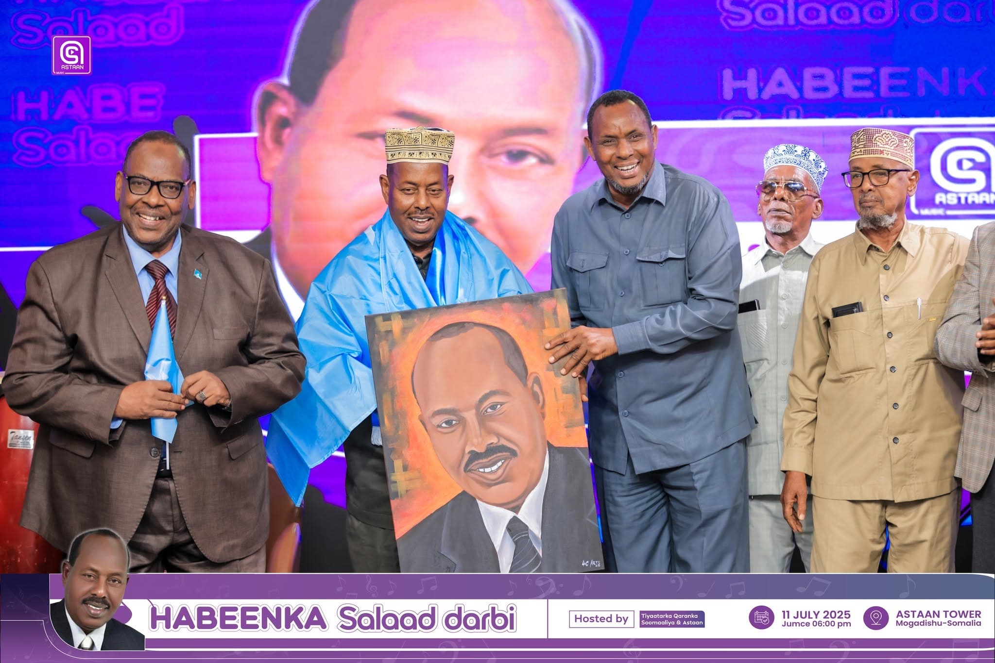 Guests on the Habeenka Salaad Darbi stage presenting a framed portrait painting of Salaad Darbi under blue ceremonial drape.