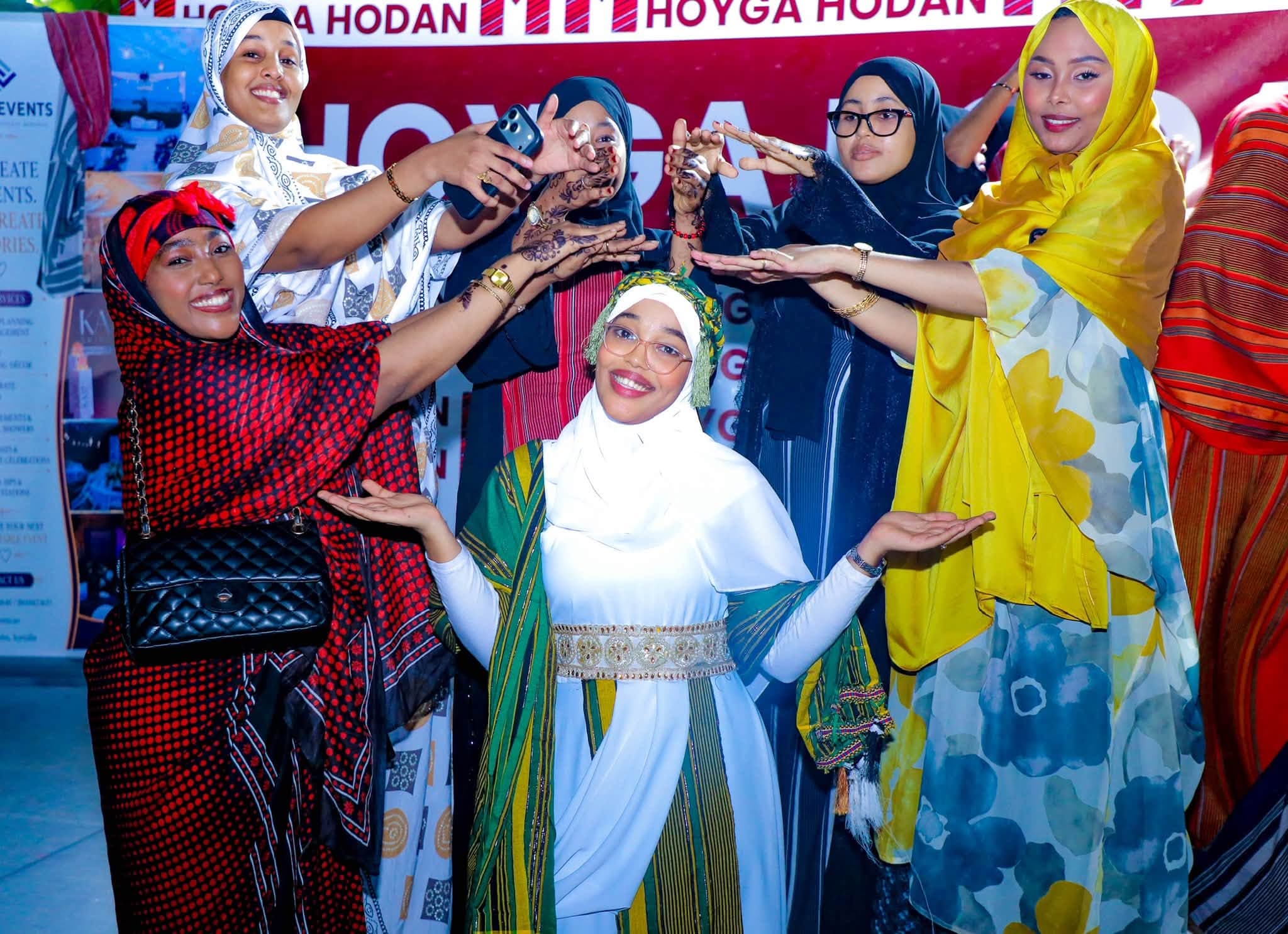 A smiling young woman in a white guntiino is celebrated by friends framing her with raised hands