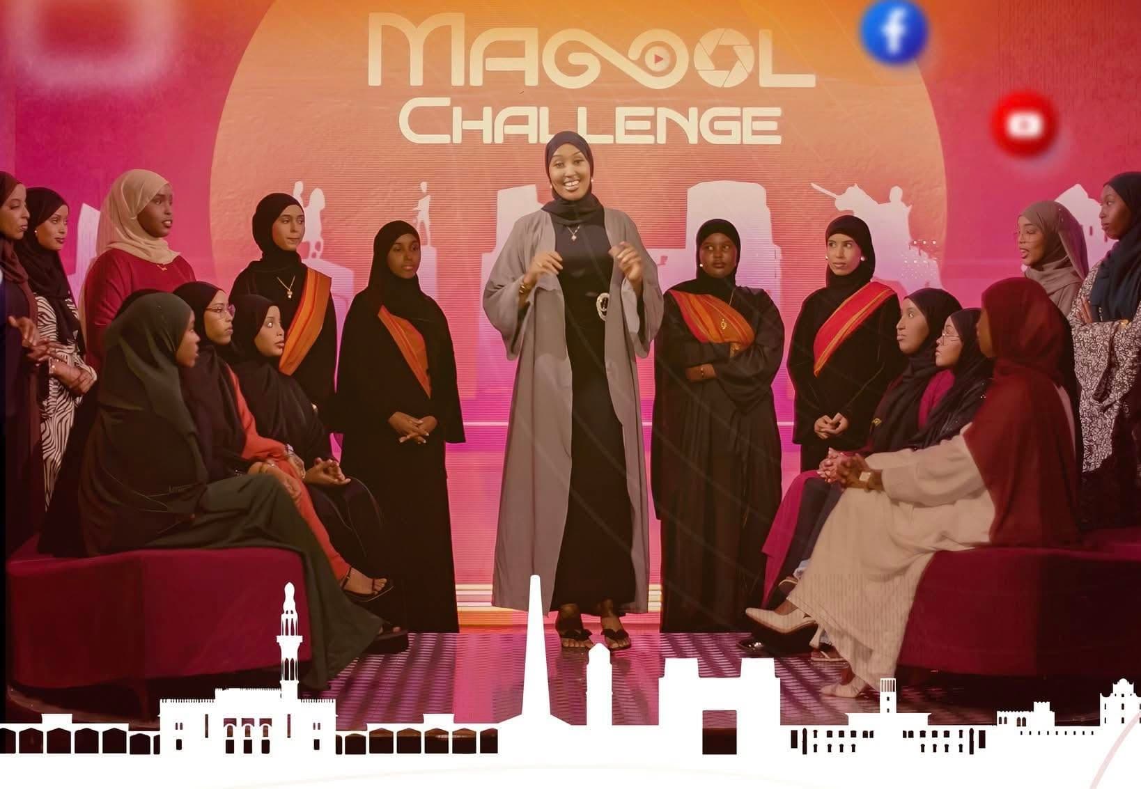 Magool Challenge contestants gathered on the pink-lit television studio set beneath the show's logo, with the presenter standing at the center in a grey abaya