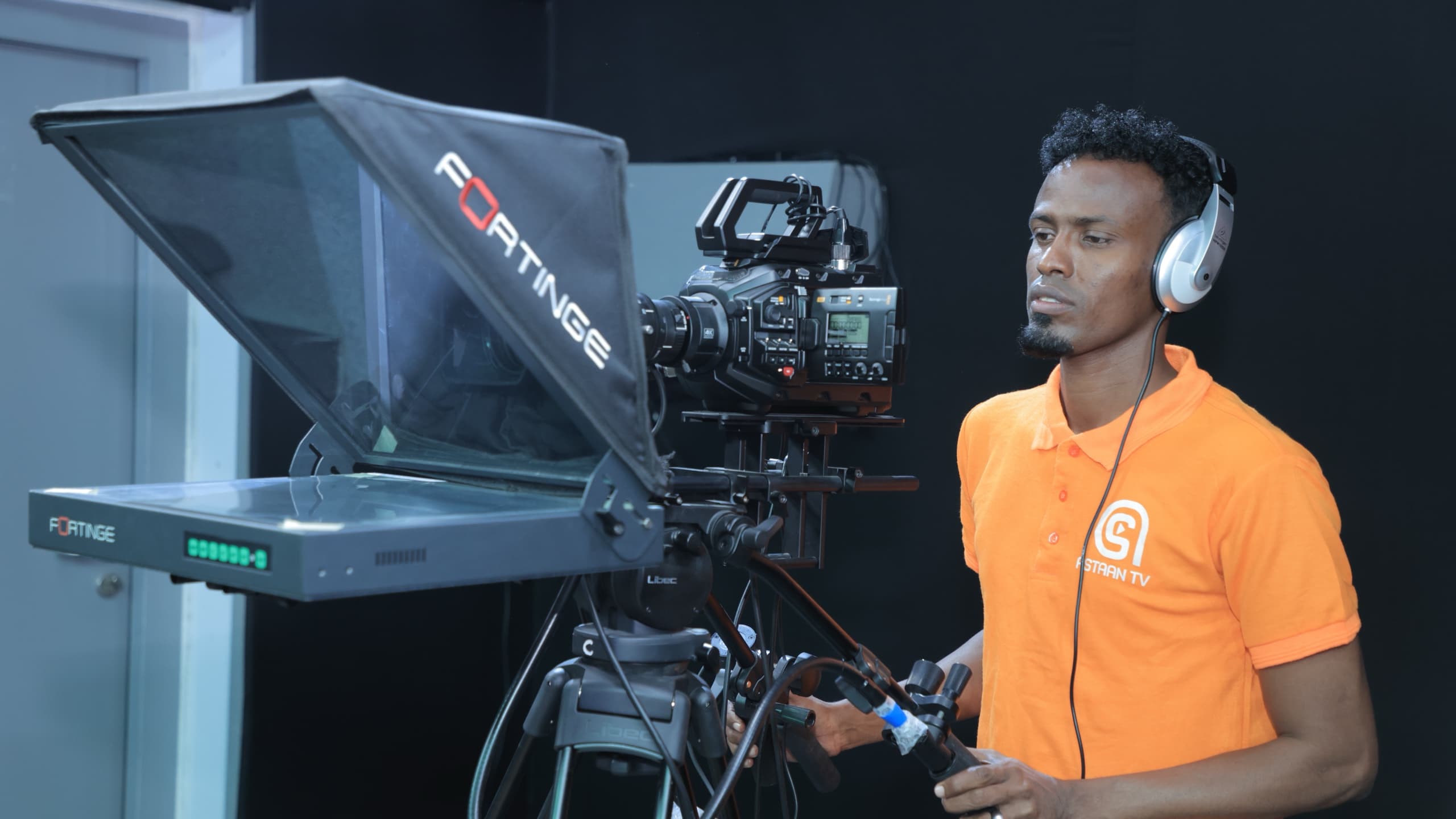 Astaan TV camera operator in headphones at a studio camera and teleprompter rig
